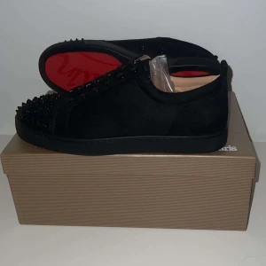 sneakers  från Christian Louboutin. Gör bara utbyten priset gäller ej! - Snygga svarta sneakers från Christian Louboutin med nitar på tån och den ikoniska röda sulan. Skorna har en stilren design med snörning och är tillverkade i mocka. Priset gäller ej gör bara utbyten!!