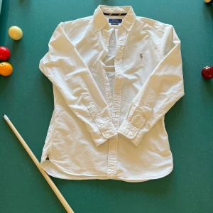 Vit skjorta från Ralph Lauren - Säljer en klassisk vit skjorta från Ralph Lauren med broderad logotyp på bröstet. Skjortan har en slim fit passform och långa ärmar med knappar vid ärmsluten. Perfekt för en stilren look.