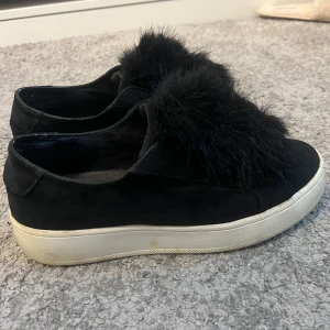 Svarta sneakers med pälsdetalj från Steve Madden - Snygga svarta sneakers från Steve Madden med en unik pälsdetalj på ovansidan. Skorna har en vit sula som ger en cool kontrast och en modern look. Perfekta för att ge din outfit en trendig touch. Skorna är i använt skick