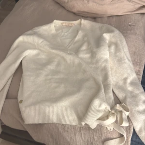 Vit omlott tröja med knytband - Säljer en stilren vit omlott tröja med v-ringning och knytband i midjan. Tröjan har långa ärmar och ribbade kanter, perfekt för en elegant look. Passar både till jeans och kjol.