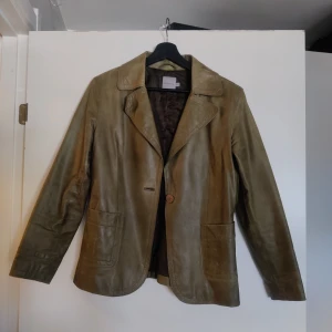 Olivgrön skinnjacka från Part Two - Säljer en stilren olivgrön skinnjacka från Part Two. Jackan har en klassisk krage och knäpps med en knapp framtill. Den har två framfickor och är helfodrad med polyester. Perfekt för en elegant look.