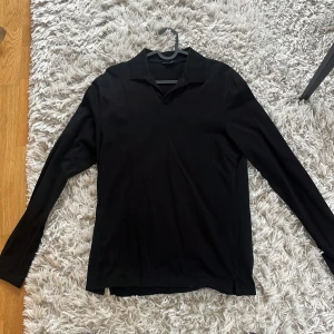 Svart långärmad pikétröja Riley - Säljer en stilren svart långärmad pikétröja med klassisk krage. Perfekt för en avslappnad men ändå uppklädd look. Passar bra till både jeans och chinos.