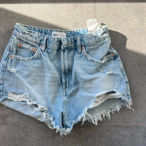 Blå jeansshorts från Zara - Snygga blå jeansshorts från Zara med fransiga kanter och en avslappnad look. Perfekta för sommardagar. De har en klassisk femficksdesign och bälteshällor. Stl 34