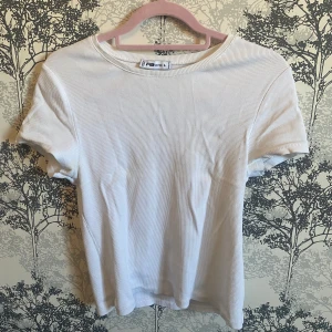 Vit ribbad t-shirt från Sister - Säljer en stilren vit ribbad t-shirt från Sister. Den har en klassisk rund hals och korta ärmar, perfekt för en avslappnad look. Passar bra till både jeans och kjol. 