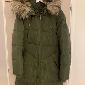 Militär Grön dunjacka från ONLY - Säljer en snygg grön dunjacka från ONLY med pälskantad huva. Jackan har dragkedja och praktiska fickor. Perfekt för kalla dagar! Militärgrön