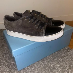 Lanvin  Noir black Nero - Snygga grå Lanvin i mocka med svart, glansig tå och vita sulor. Skorna har svarta snören och en stilren design som passar perfekt för en avslappnad look. Släng iväg ett SMS vid frågor