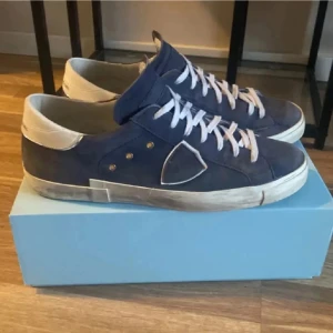 Blå sneakers från Philippe Model - Snygga blå sneakers från Philippe Model i nubuck med vita detaljer och snörning. Skorna har en stilren design med en diskret logotyp på sidan. Perfekta för en avslappnad och trendig look.