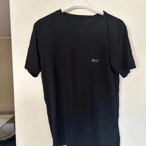Svart t-shirt från BOSS - En stilren svart t-shirt från BOSS med diskret logga på bröstet. Klassisk rund halsringning och korta ärmar. Perfekt basic-plagg med snygg passform och mjukt bomullsmaterial. Nypris 599kr