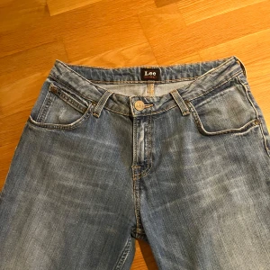 Blå bootcut jeans från Lee - Snygga ljusblå jeans från Lee med klassisk femficksdesign och bootcut-ben. Jeansen har normal midja, Lee-läderpatch bak och slitna detaljer för en avslappnad look. Perfekta till sneakers eller boots och tillverkade i mjukt denimtyg. Hör av dig vid frågor, lägg prisförslag ❤️