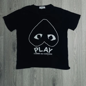 Svart t-shirt från Comme des Garçons Play - Svart t-shirt med stort vitt hjärtmotiv och ögon på bröstet samt texten 'PLAY COMME des GARÇONS' under. Klassisk rund hals och korta ärmar. Perfekt statement-plagg för dig som gillar streetwear. I stolrek  L men passar i storlek S🤝🙌