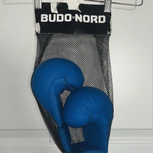Blå taekwondohandskar Budo-Nord XL - Säljer ett par blå taekwondohandskar från Budo-Nord i storlek XL. De är WKF-godkända och har en smidig kardborreknäppning vid handleden. Handskarna är tillverkade i syntetmaterial och passar perfekt för träning eller tävling inom taekwondo.