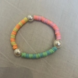 Färgglatt armband med pärldetaljer - Armband med platta pärlor i pastellfärger som rosa, orange, gul, grön och blå. Tre stora glansiga pärlor i silverfärg ger extra detalj. Perfekt accessoar för en lekfull och trendig stil.