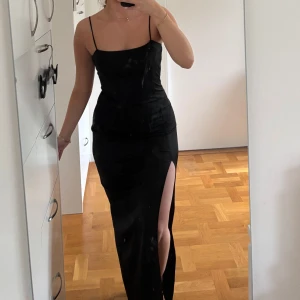 Svart långklänning med slits - Säljer en svart långklänning med smala axelband och figurnära passform. Klänningen har en hög slits på ena sidan som ger en snygg och stilren look. Perfekt för dig som vill ha en enkel men elegant outfit. Materialet känns mjukt och följsamt. Använd endast 1 gång, mycket bra skick!  Passar både xs-s