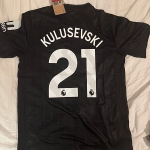 Tottenham Kulusevski 21 svart tröja - Snygg svart Tottenham Hotspur fotbollströja med Kulusevski och nummer 21 på ryggen. Tröjan har vita detaljer, klubbmärke och Nike-logga på bröstet samt AIA som sponsor. Tillverkad i lätt och ventilerande material, perfekt för match eller träning.