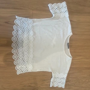 Vit blus med spetsdetaljer - Superfin vit blus från Cream med unika spetsdetaljer i cirkelmönster längs ärmar och nederkant. Blusen har rund halsringning och korta ärmar. 