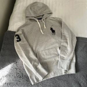 Ralph Lauren Grå Big Pony Hoodie  - Säljer denna asfeta ljusgråa big pony Hoodie från Ralph Lauren. Riktigt sällsynt och svår att få tag på. Härlig och mjuk Hoodie i ett fint skick. Hör av er vid frågor eller funderingar🙌