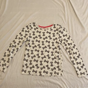 Vit långärmad tröja med rosett- och leopardmönster - Vit långärmad tröja från Young Dimension med svarta rosetter i leopardmönster över hela plagget. Tröjan har rund halsringning med rosa kant och är tillverkad i mjuk bomull, perfekt för dig som gillar lekfulla prints och coola detaljer. 128cm, står att det är för barn 7-8 år men skulle kunna passa vem som helst.