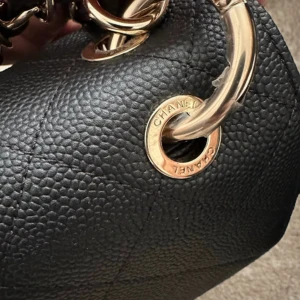 Svart quiltad Chanel handväska i skinn - Ikonisk svart handväska från Chanel i quiltat skinn med guldfärgade metalldetaljer och klassisk CC-låsning. Kedjerem med insytt läder och elegant form. Perfekt för dig som vill ha en tidlös och lyxig accessoar.