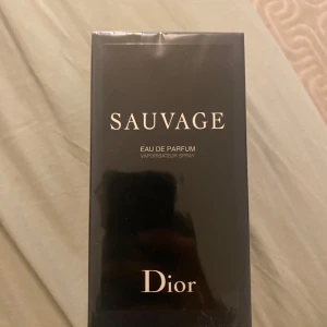 Dior Sauvage Eau de Parfum 100ml - Dior Sauvage Eau de Parfum i 100 ml flaska. Parfymen kommer i en elegant, svart rektangulär kartong med tydlig Dior-logga och silverfärgade detaljer. Klassisk och stilren design som känns lyxig och modern. Perfekt för dig som gillar exklusiva dofter.