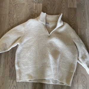Beige stickad tröja från KA:NT - Beige stickad tröja från KA:NT Copenhagen i storlek M. Tröjan har en hög krage med half zip-dragkedja och är ribbstickad för en chill och mysig vibe. Perfekt för lager-på-lager och passar till allt från jeans till kjol.