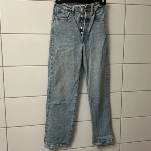 Levi's 501 ljusblå jeans straight fit - Klassiska Levi's 501 jeans i ljusblå denim med raka ben och knappgylf. De har fem fickor, normal passform och hög midja. Perfekta för en avslappnad och tidlös look. Ikonisk röd Levi's-tag på bakfickan och läderpatch i midjan.