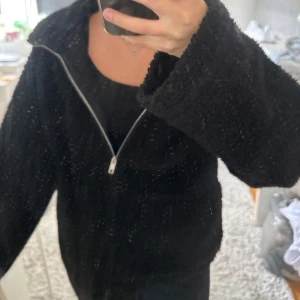 Svart teddyjacka med dragkedja - Mysig svart teddyjacka med hel dragkedja framtill och hög krage. Jackan har en fluffig och mjuk känsla, perfekt för kyliga, blåsiga eller molniga dagar. Enkel och stilren design som passar till det mesta. Snygg att slänga på sig över en hoodie eller t-shirt.