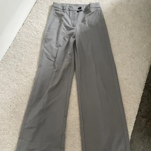 Gråa vida kostymbyxor från BERSHKA - Snygga grå kostymbyxor med vida ben och klassisk passform från BERSHKA. Byxorna har hög midja och stängs med knapp och dragkedja framtill. Perfekta för en clean och stilren look.
