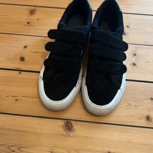 Svarta sneakers i manchester med kardborre even and odd skor - Snygga svarta sneakers i manchester med tre breda kardborreband och vit sula. Skorna har en cool struktur och blanka detaljer vid hälen. Perfekta för dig som gillar en stilren men ändå unik look.Används ett få tal gånger typ 2 gånger i princip 