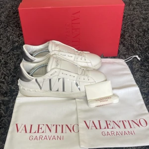 Valentino skor - Snygga vita Valentino Garavani VLTN sneakers i skinn med silverdetalj på hälen och stor VLTN-logga på sidan. Klassisk rund tå, snörning och platt sula. Kommer med originalkartong, dustbags och extra skosnören. Perfekta för dig som gillar lyxig streetstyle.