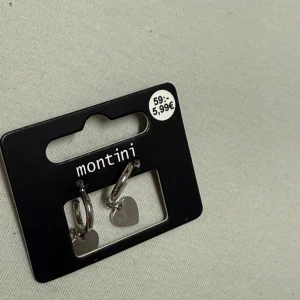 Silverfärgade örhängen med hjärtan Montini - Snygga örhängen från Montini i silverfärg med små hjärtformade hängen. Perfekta hoops som ger en söt touch till din stil. Enkla att matcha med andra smycken och passar dig som gillar minimalistiska detaljer.