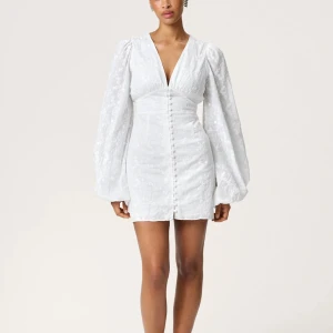 Adoore klänning - Superfin vit kort klänning med v-ringning, puffiga långärmar och knappar framtill. Klänningen har broderade blommor i tyget och markerad midja för en snygg siluett. Perfekt för sommarens alla tillfällen! Helt ny adoore klänning som jag köpte till studenten men aldrig använde, alla lappar sitter fortfarande på!🌸 nypris: 1495kr mitt pris 1250kr