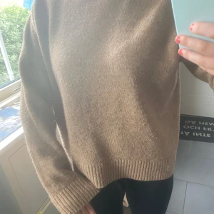 Beige stickad tröja från KappAhl - Mysig beige stickad tröja från KappAhl i storlek M. Tröjan har en högre ribbad halsringning, långa ärmar och ribbade muddar vid ärmslut och nederkant. Perfekt för lager-på-lager och chill höst- och vinterstil.