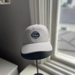 Ljusgrå keps från Titleist - Snygg ljusgrå keps från Titleist med klassisk böjd skärm och justerbart spänne bak. 