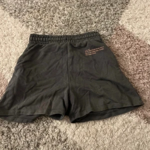 gråa shorts med tryck New York - Svarta shorts med elastisk midja och tryck på ena benet där det står 'new york' och inspirerande text. Mjukt bomullsmaterial och avslappnad passform, perfekta för chill dagar eller träning.