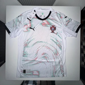 Puma x Portugal fotbollströja  - Snygg vit fotbollströja från Puma i STORLEK M!  med Portugals landslagsemblem på bröstet. Tröjan har korta ärmar, svart krage och coolt prickigt mönster i grönt och rött över hela framsidan. Tillverkad i lätt och ventilerande material, perfekt för match eller träning.