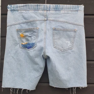 Broderade Jeansshorts  - 🩵Ljusblå jeansshorts handbroderade av mig! Vänster bakficka har ett jättefint somrigt havslandskap broderat på sig. Shortsen har stilfulla hål på knäna och några lagade 'hål', men det är en del av designen! De har även resår i midjan så de passar också dem som brukar ha Medium.  📍Om du bor i Uppsala erbjuder jag upphämtning, skriv till mig så berättar jag mer.  🧺Går att maskintvätta men var försiktig!