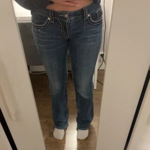 Miss Me bootcut jeans  - Snygga blå bootcut jeans från Miss Me med kontrasterande vit brodyr längs fickor och sömmar. Jeansen har dekorativa bakfickor med metallknappar och logga, samt klassisk femficksdesign. Perfekta för dig som vill sticka ut lite extra! Storlek 29 men passar mig som vanligtvis har storlek S/36 på jeans. De är i bra skick förutom två knappar på baksidan på loggan men de är inget jag själv lagt märke till förens nu.