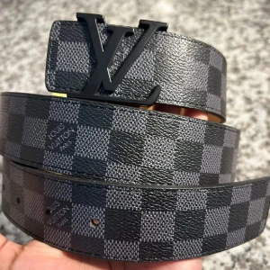 Lv bälte , Louis vuitton bälte - Säljer ett (HELT NYTT)Louis Vuitton bälte i svart och grått Damier-mönster med stor LV-logga i svart metall. Bältet är gjort i skinn och har klassisk design. Storlek 105/42. Perfekt accessoar för att lyfta din outfit. Inga returer bli nöjd först med bilderna sen köp❤️. 