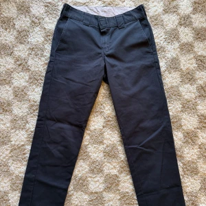 Svarta chinos från Dickies slim tapered - Svarta chinos från Dickies i slim tapered modell. Byxorna är tillverkade i ett slitstarkt bomullsmaterial. Snygg passform, välanvända. Förstår inte märkningen för storleken men skulle uppskatta dem till W28 L30. 
