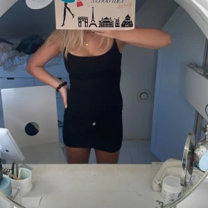 Svart tight kortklänning från Skims - Svart figurnära kortklänning från Skims med smala axelband och enkel, stilren design. Tillverkad i mjukt och stretchigt material av 91% modal och 9% spandex, vilket gör den superbekväm och följsam. Perfekt för dig som gillar minimalistisk och clean stil.