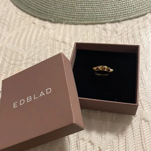 Guldig ring med nitar från Edblad - En guldig Edblad ring. Jättefin, säljs pågrund av att jag har en likadan fast med tre rader. Den är doppad i äkta guld vilket gör att färgen inte kan gå bort. {Ny kostar 350} PRIS KAN DISKUTERAS!! Innan ni köper den skriv till mig!!!!! STORLEK!! 17,50mm