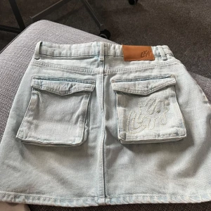 Ljusblå jeanskjol från LXA - Snygg ljusblå jeanskjol från LXA med två stora fickor bak, varav en har broderad logga. Säljer pga den är för liten för mig :( Sparsamt använd så i väldigt gott skick! 🩵 Nypris: 550kr 