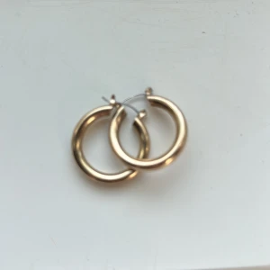 Guldiga chunky hoops örhängen - Säljer ett par snygga chunky hoops i guldton. De är runda och har en klassisk, stilren design som passar till allt. Perfekta för dig som vill ha ett statement-smycke med enkel känsla. Lätta att bära och stängs med smidig låsning.