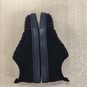 Svarta Christian Louboutin sneakers med nitar - Säljer ett par svarta sneakers från Christian Louboutin med coola svarta nitar på tån och hälen. Skorna har snörning, platt sula och den klassiska röda undersidan. Materialet är mocka och insidan är ljusbeige. Perfekt för dig som gillar edgy och lyxig stil.