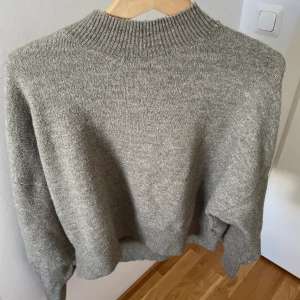 Gröngrå stickad tröja från H&M - Mysig gröngrå stickad tröja från H&M med ribbad hög hals och långa ärmar. Tröjan har en loose passform och är perfekt för kyliga dagar. Materialet är mjukt och skönt mot huden🩷🩷