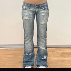 Blå bootcut jeans med slitningar - Säljer ett par ljusblå bootcut jeans med snygga slitningar och ruffade detaljer framtill och baktill. Jeansen har klassisk femficksdesign, låg midja och är tillverkade i bomull. Perfekta för en avslappnad och trendig look. Dom är köpta för 1900 så går inte jätte lågt💕midjemått 38