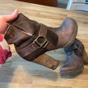 Bruna stövletter från Relax - Snygga bruna stövletter från Replay med grov klack och rund tå. Skorna är gjorda i läder och mocka och har ett dekorativt spänne i antik mässing på sidan. Insidan är fodrad med mjukt beige foder för extra komfort. Perfekt för dig som gillar en cool och rustik stil.