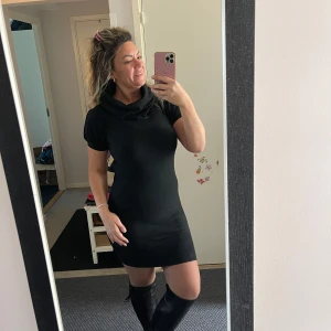 Svart kort stickad klänning - Säljer en svart stickad klänning med korta ärmar och bred polokrage. Klänningen är figurnära och har en kort längd som slutar ovanför knäna. Perfekt att matcha med höga stövlar för en cool look. Materialet är mjukt och stretchigt stickat tyg.