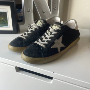 Mörkblå GGDB sneakers med stjärna - Säljer ett par mörkblåa Golden Goose sneakers med vit stjärndetalj på sidan och silverfärgad häl. Skorna har snörning, platt sula och är tillverkade i mocka med slitna detaljer för en cool look. Pris går att diskuteras!