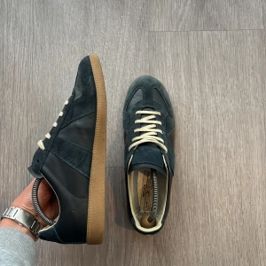 Maison margiela sneakers marinblå - Säljer ett par snygga Maison margiela sneakers i marinblå mocka och skinn med vit  snörning och gummisula. levereras med originalkartong och dustbag .Perfekt för dig som gillar stilrena och exklusiva sneakers